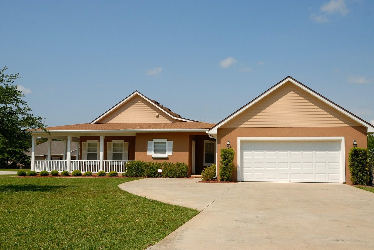 Single-story stucco home with a covered porch, a two-car garage and a green lawn under a blue sky (sample photo)